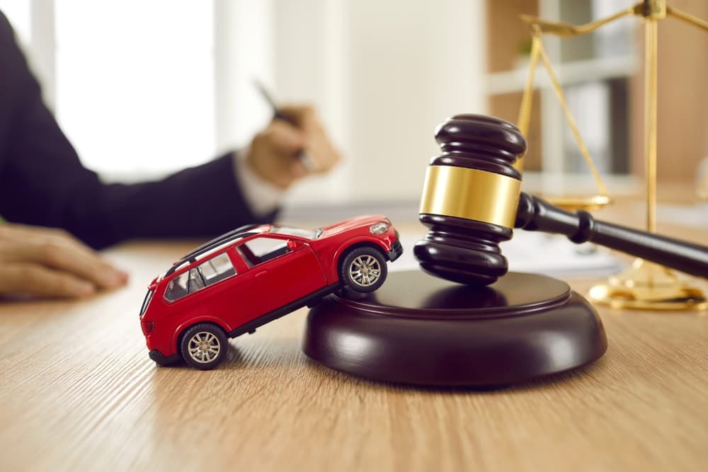 Toy car model, sound block, and gavel on a wooden desk. Symbolizes car accident, lawsuit, justice, and legal services concept.