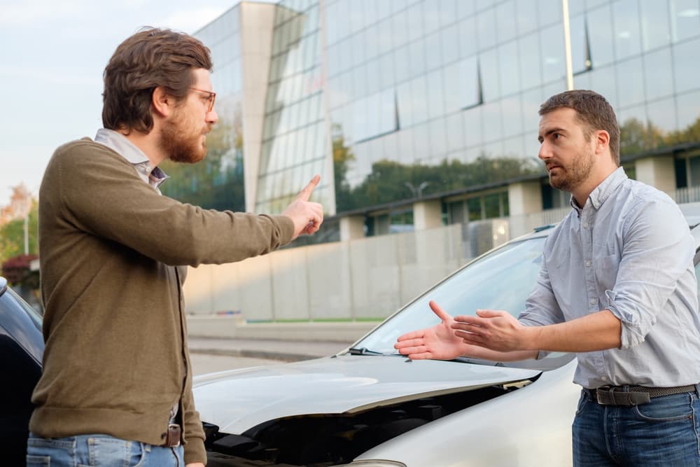 Two men engaged in a heated argument following a car accident on the road.
