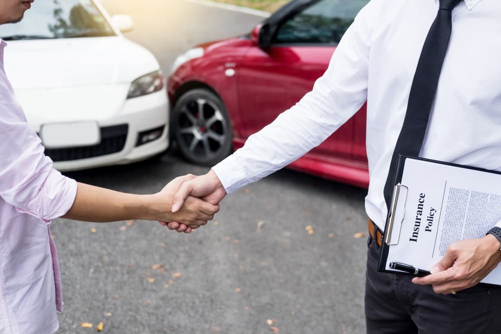 Customer shaking hands with auto insurance agents after reaching a friendly agreement on insurance terms following a car accident.