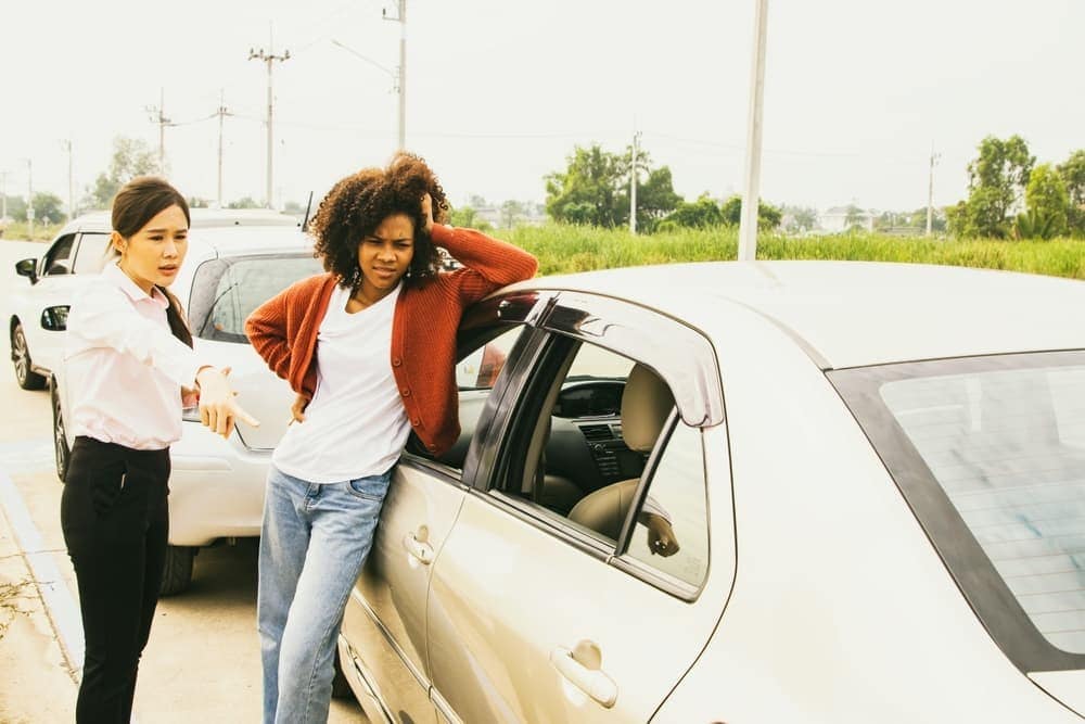 Woman inspecting brake marks after car crash on road, upset and pointing, seeking compensation from other driver. Car insurance concept.