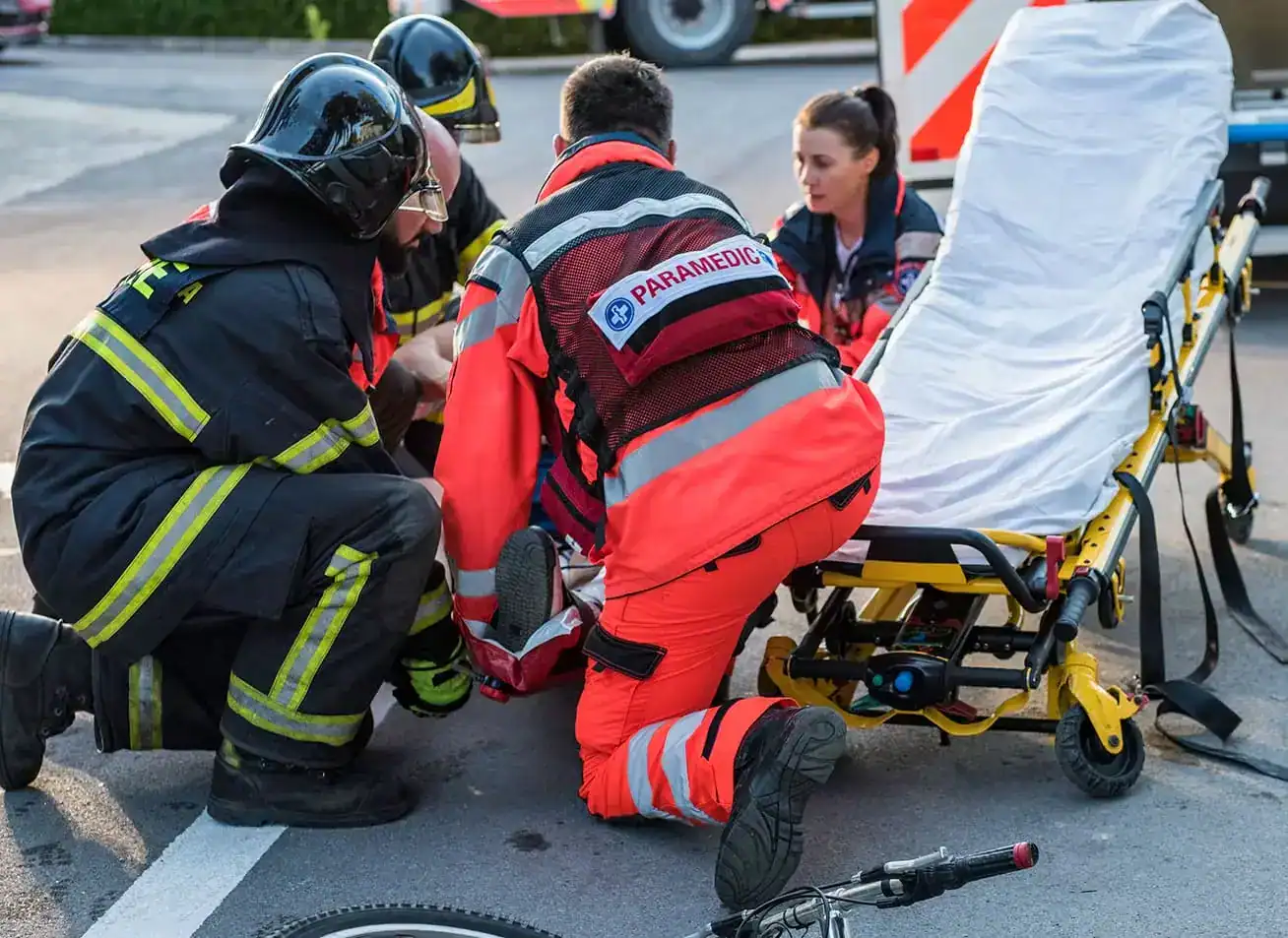 Paramedics and firefighters helping injured cyclist after bicycle accident with stretcher on road.