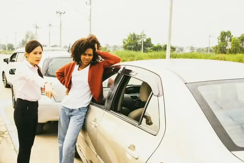 Two female drivers inspecting and discussing vehicle damage after a car accident on the road.