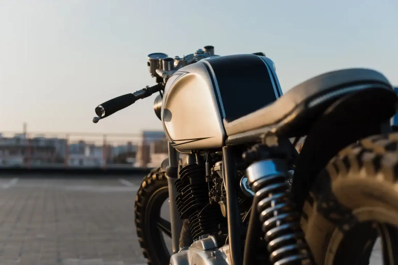 Close-up view of a retro-style motorcycle parked in the city with urban background at sunset.