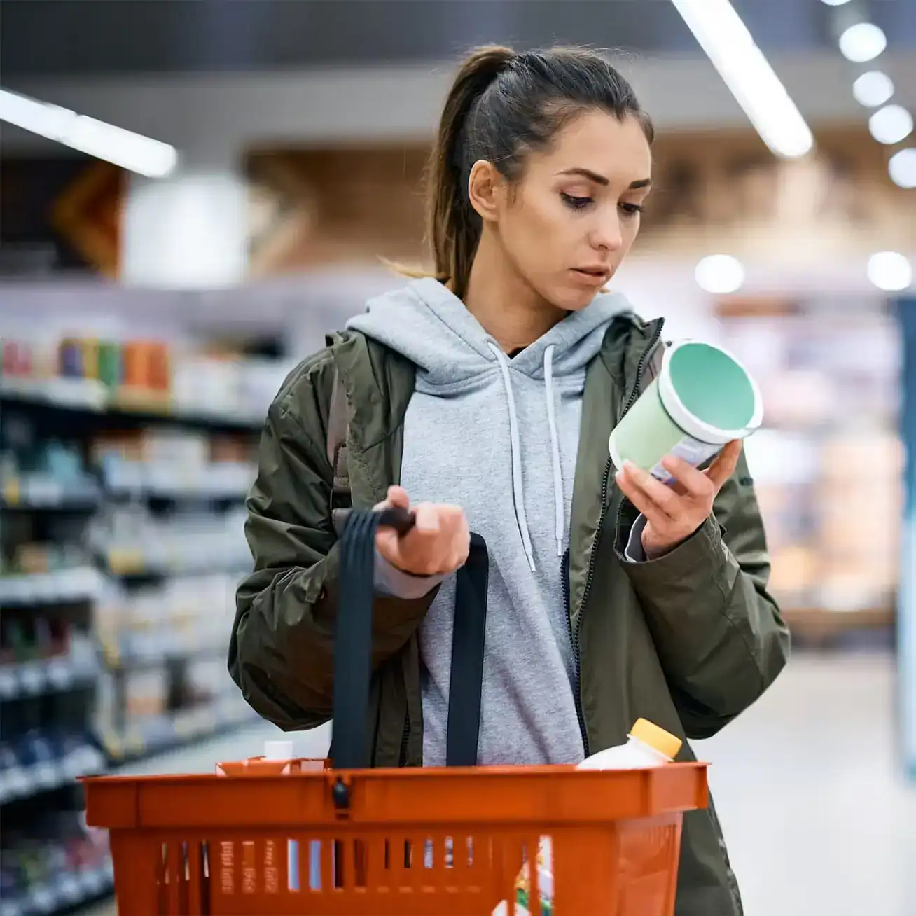Woman shopping in grocery store reading product label while holding basket