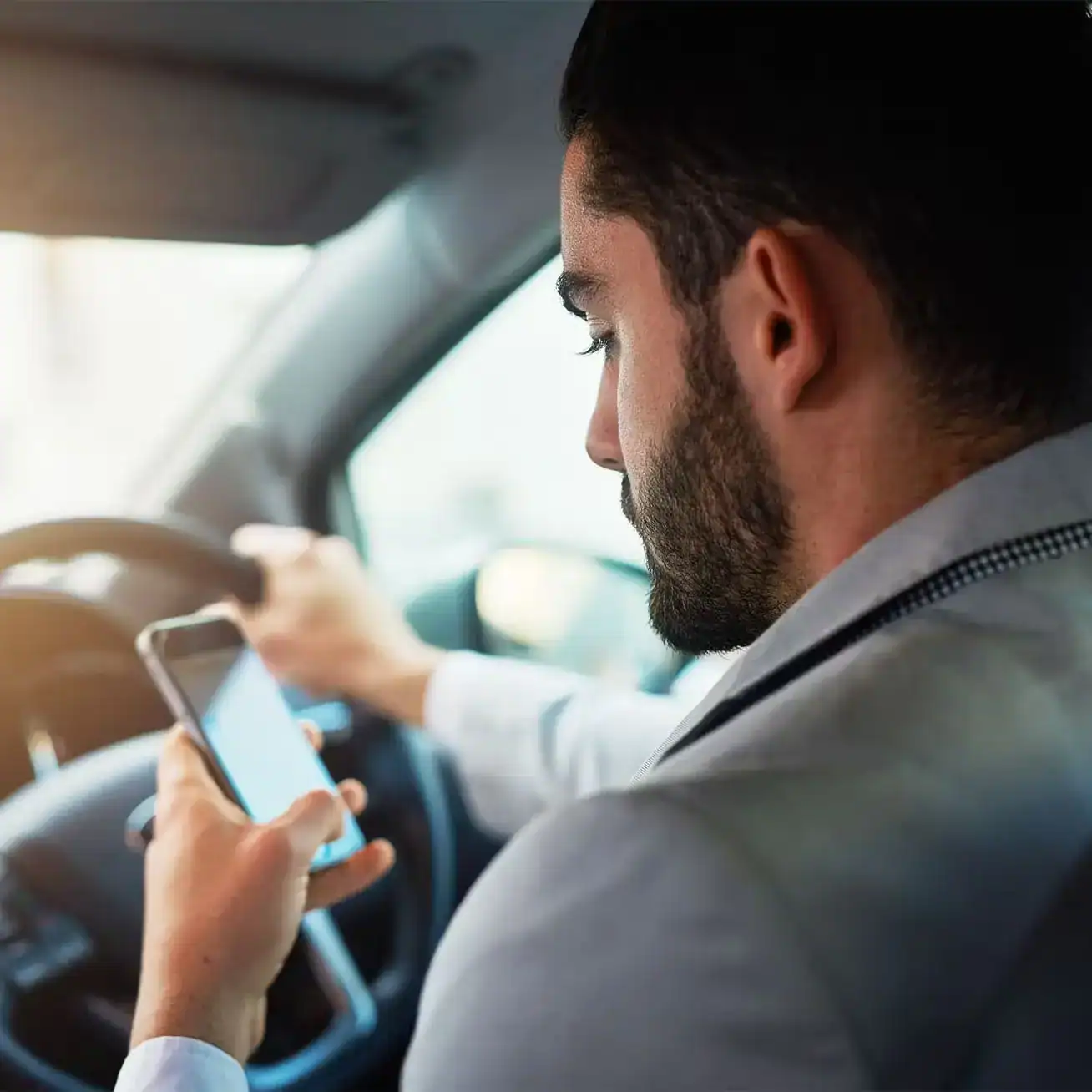 Man driving while texting on his phone, representing distracted driving accident risk.
