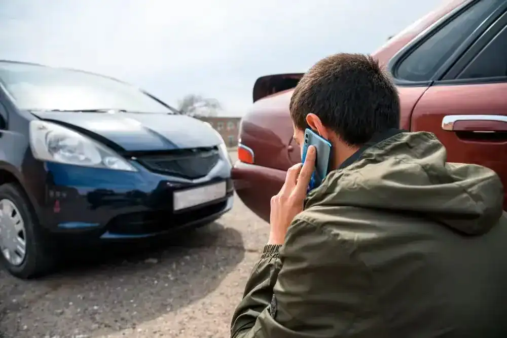 Man calling insurance company after minor car accident with two damaged vehicles.