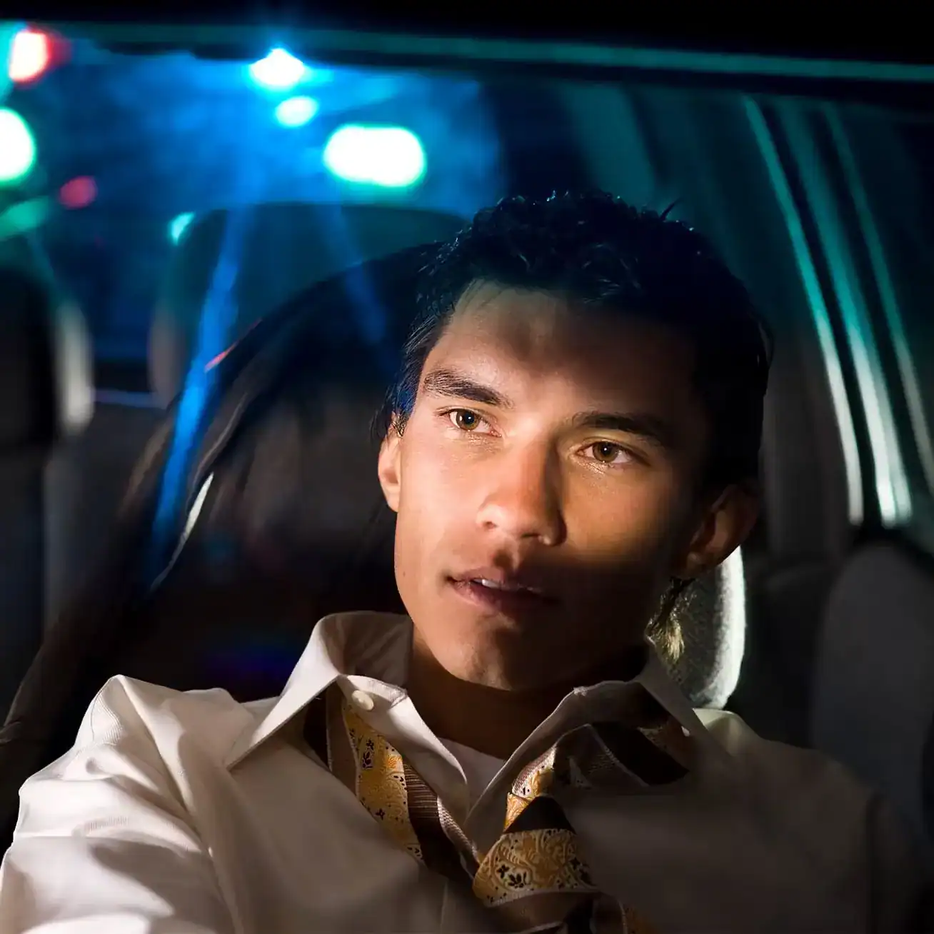 Man in car pulled over by police for suspected DUI with flashing lights in background.