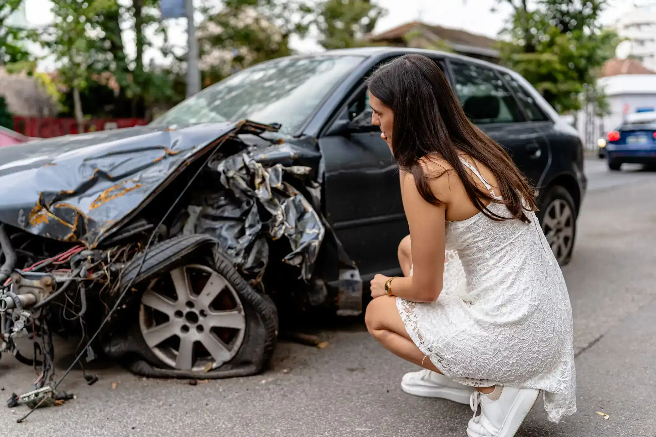 Woman inspecting heavily damaged car after crash, representing the need for experienced Houston car accident lawyers.