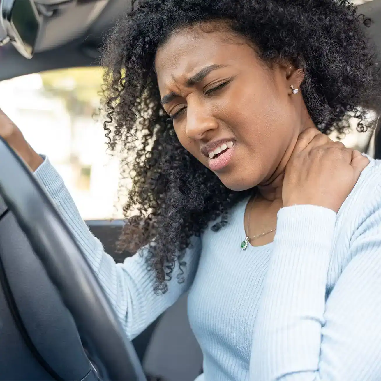 Woman in pain holding her neck after a car accident, showing signs of whiplash injury inside her vehicle.