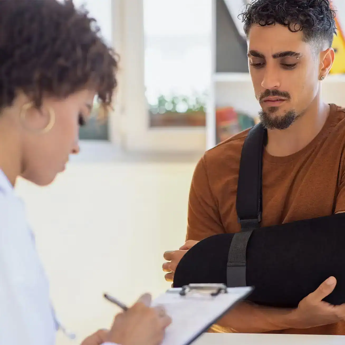 Man with an arm injury in a sling speaking to a doctor after an accident, documenting medical treatment for a personal injury claim.