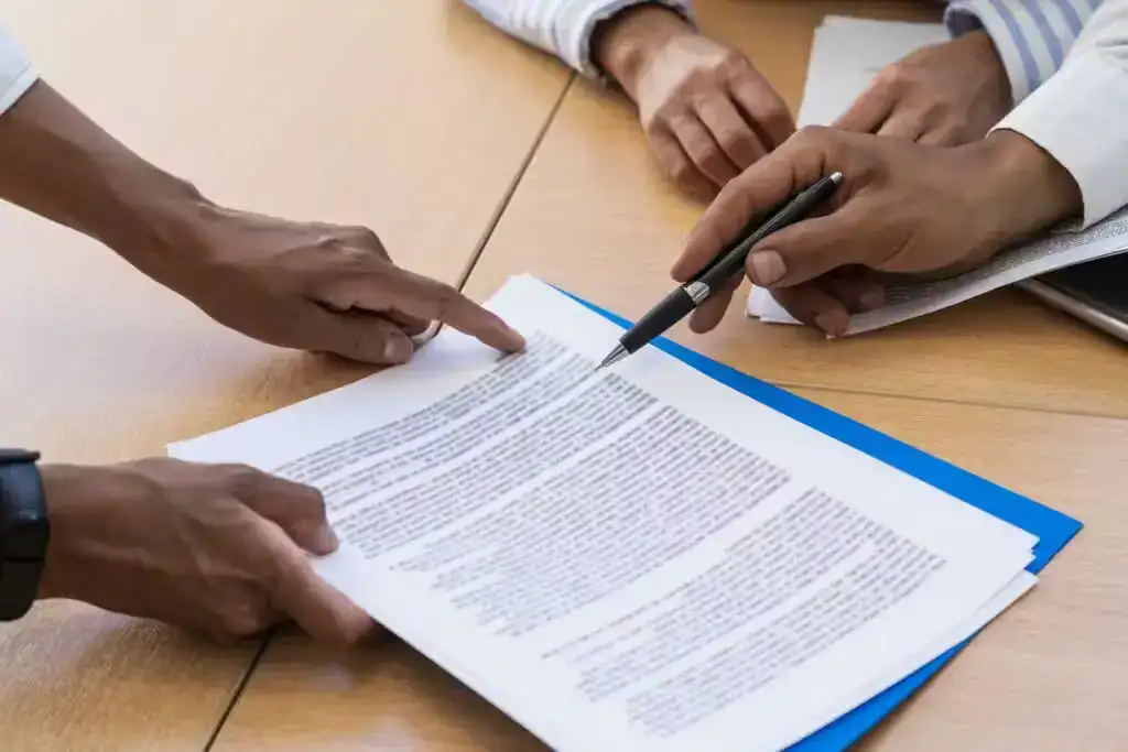 Closeup of lawyer and client reviewing legal documents and signing papers during consultation at law office.