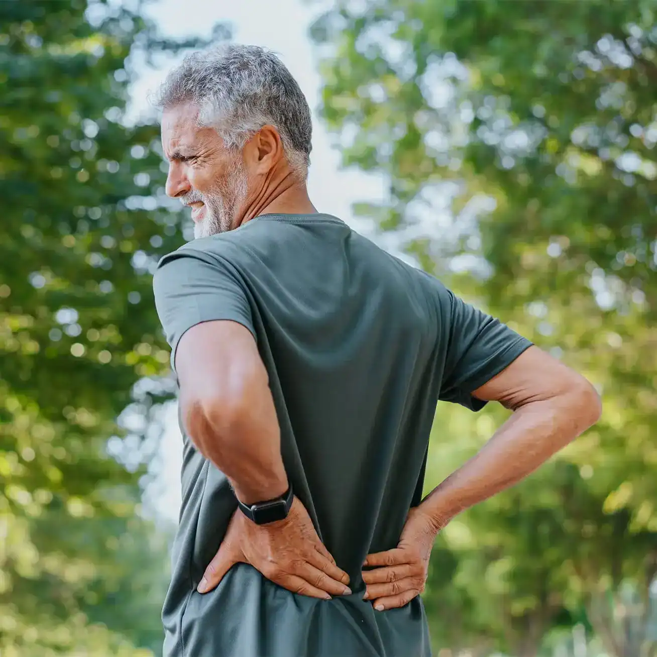 Older man outdoors holding lower back in pain illustrating personal injury or accident-related back injury