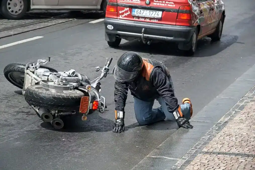 Motorcyclist injured after crash, kneeling on the road next to a fallen motorcycle.