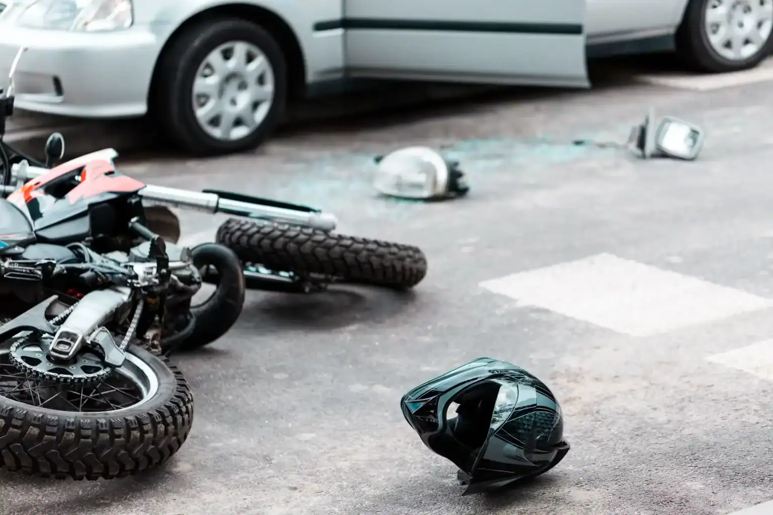Motorcycle accident with damaged bike, helmet, and car at crash site