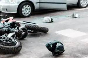 Motorcycle lying on road after collision with car, helmet and debris scattered on ground