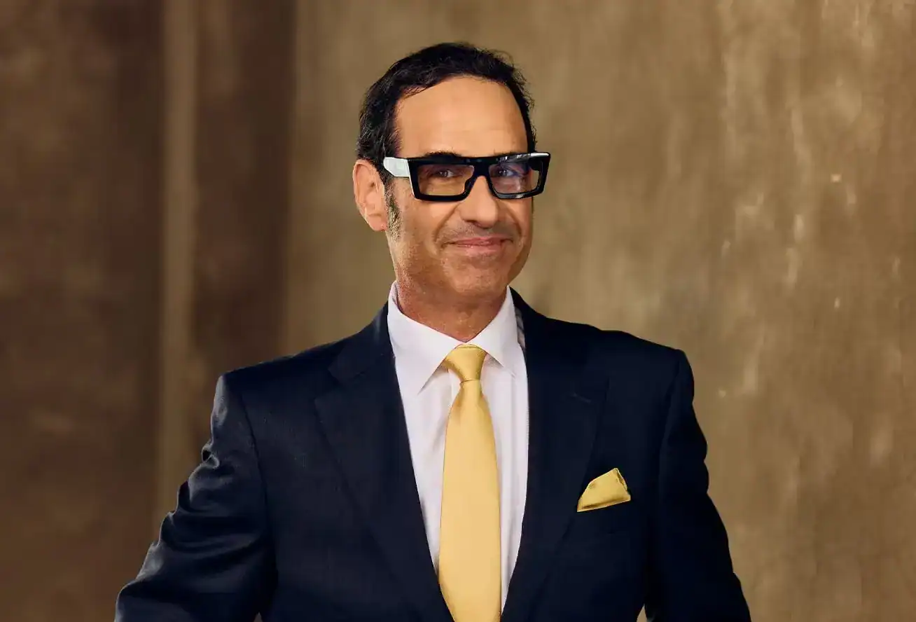 Confident personal injury attorney in dark suit with yellow tie and pocket square, standing with hands in pockets.