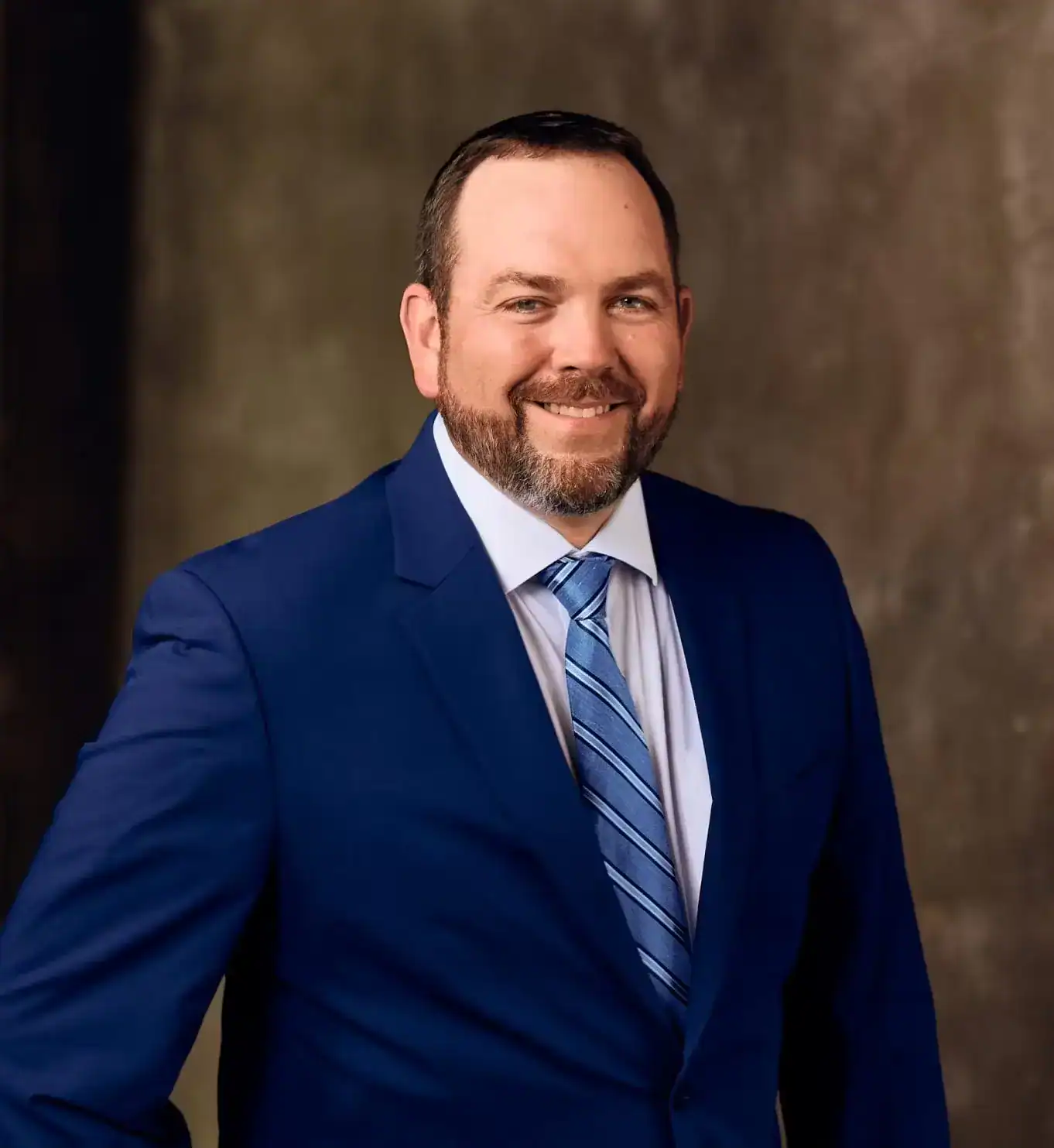 Professional portrait of a smiling lawyer in a blue suit with striped tie against a neutral background