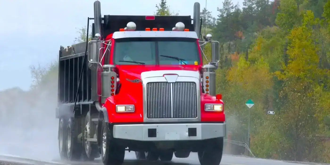 Large red semi-truck driving on a wet road, illustrating the risk of truck accidents in bad weather.
