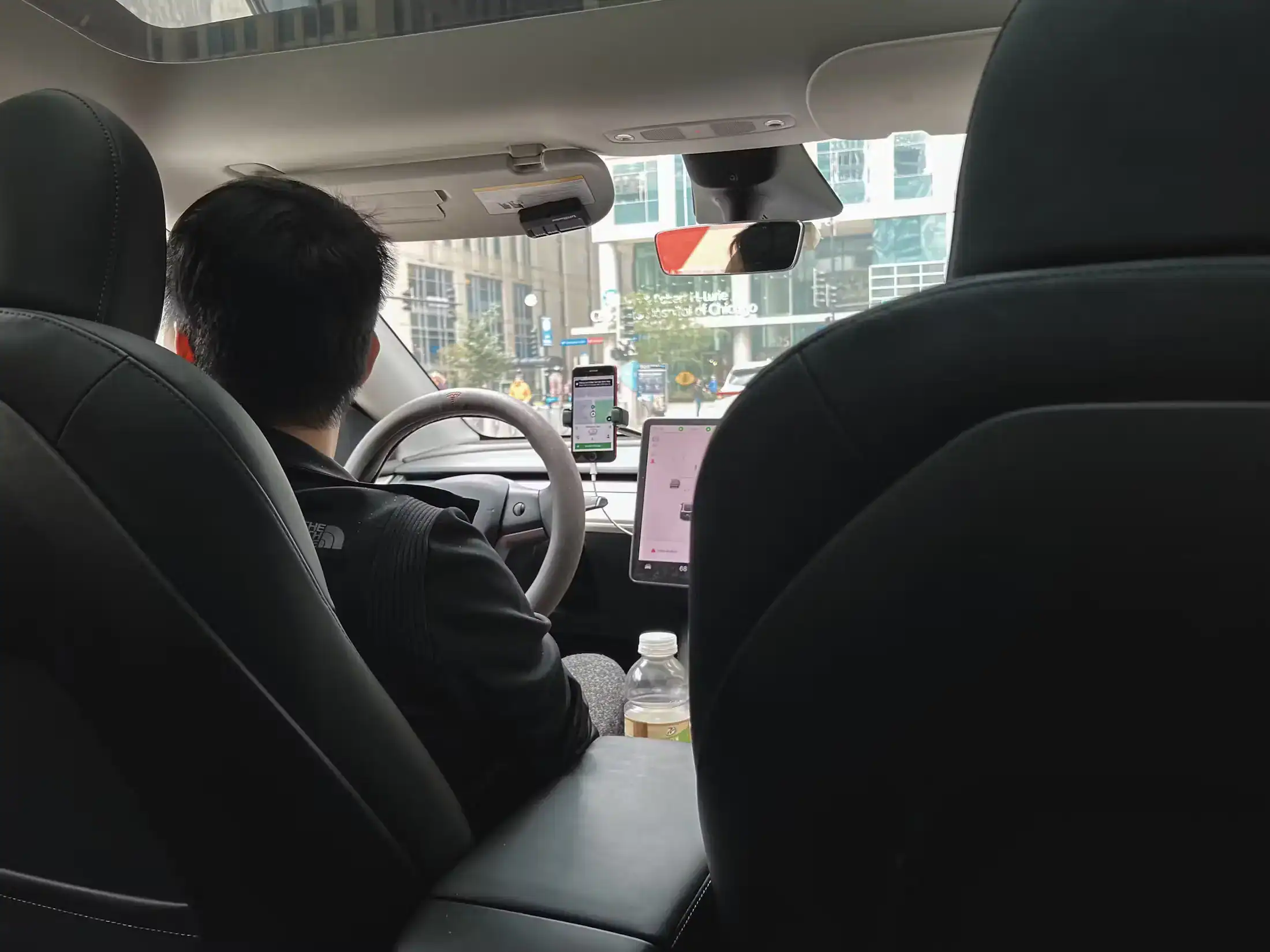 Passenger view of rideshare driver using Uber app on phone while driving in city traffic