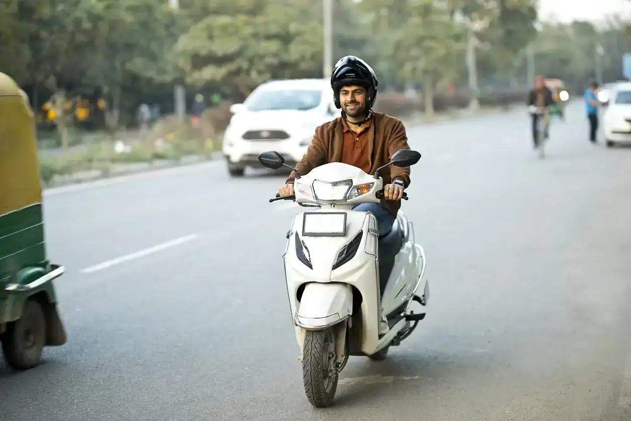Man riding scooter wearing helmet on busy city road with cars and rickshaw