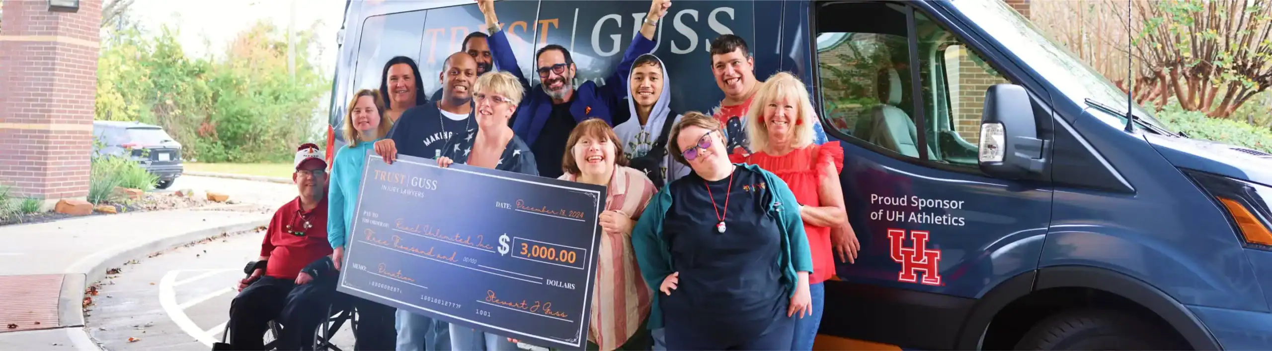 Stewart J. Guss Injury Lawyers donation presentation with community group holding $3000 check, UH Athletics sponsorship van in background