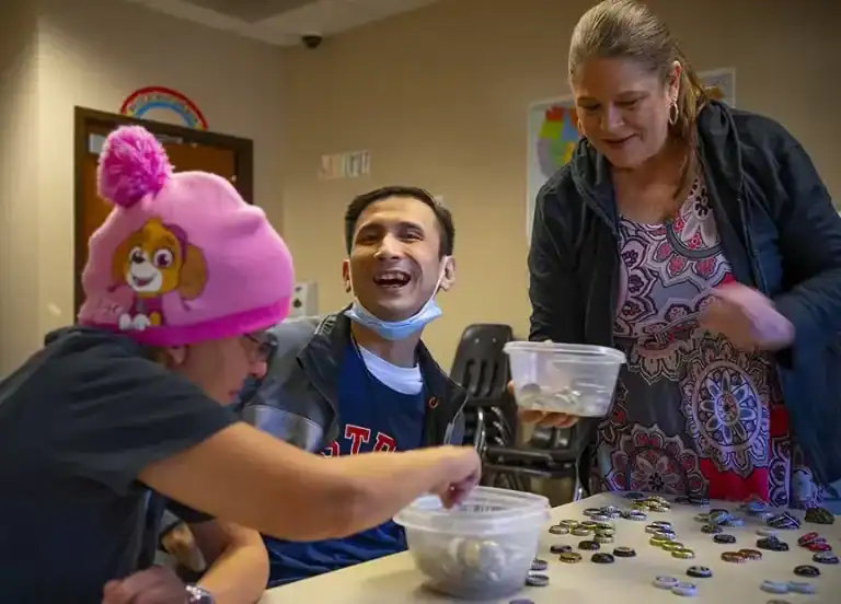 Three people smiling and sorting colorful items together at a table