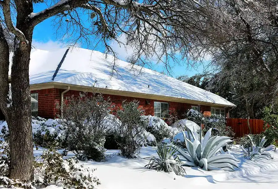 Red brick Texas home with snow-covered roof and yard after winter storm.