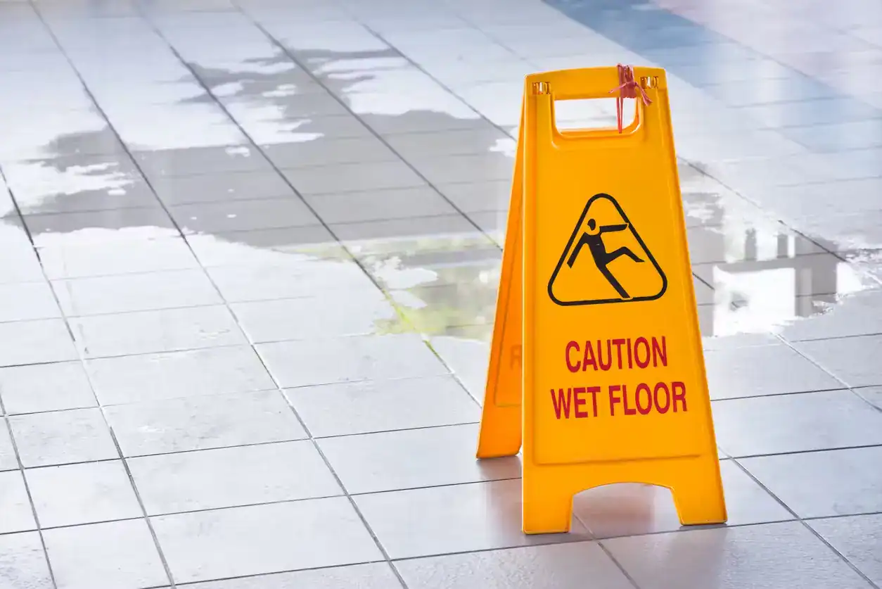 Yellow caution wet floor sign on slippery tile surface, showing potential slip and fall accident risk.