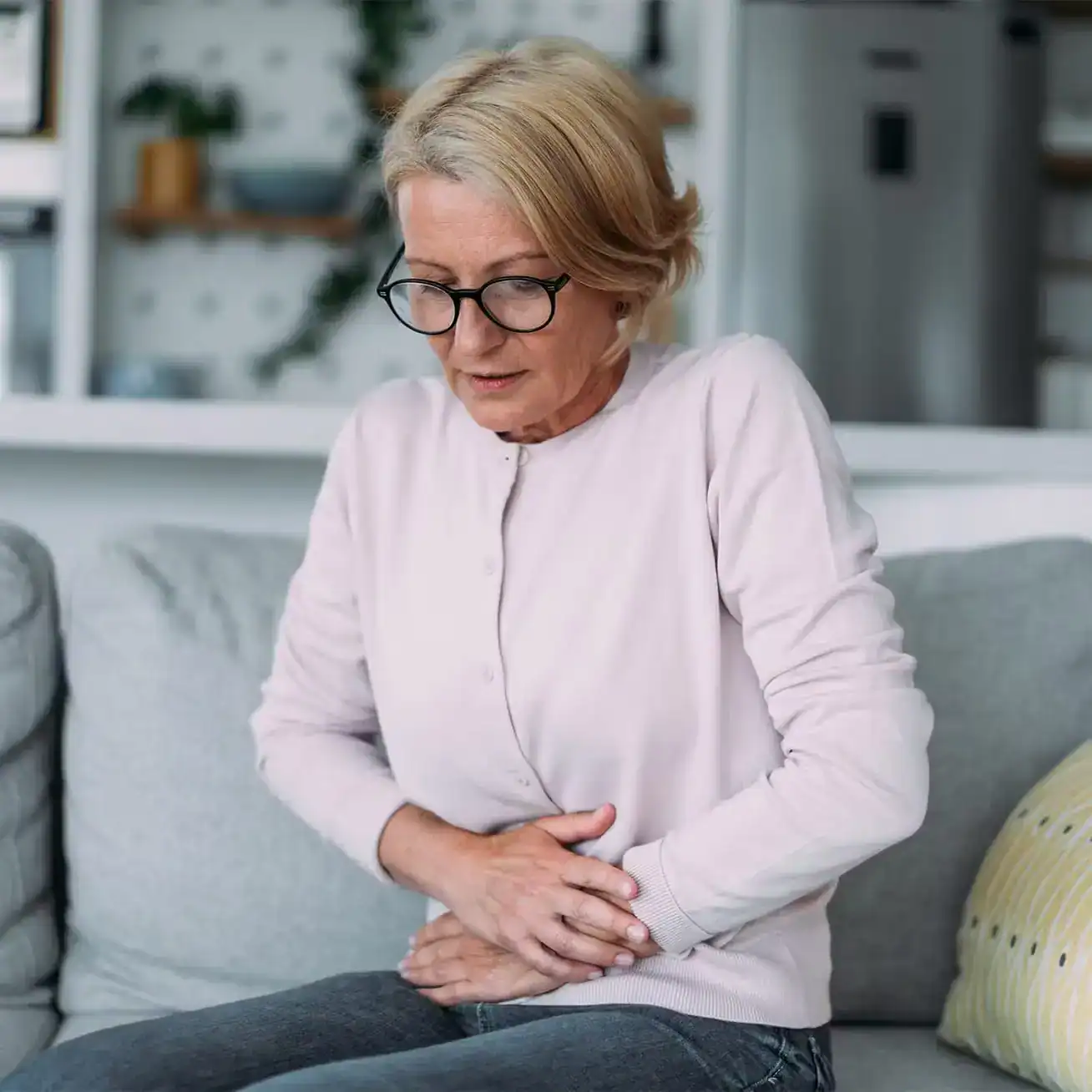 Middle-aged woman sitting on couch holding stomach in pain illustrating possible product liability or medical injury