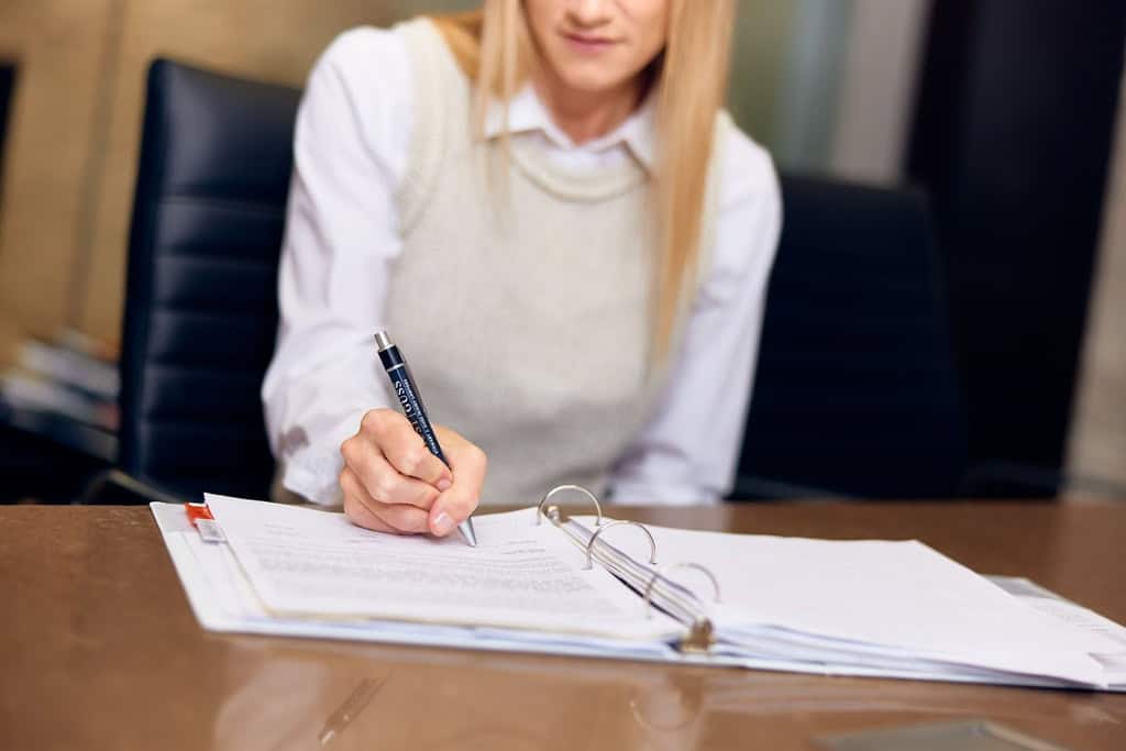 woman with long hair in a white shirt and beige vest sitting at a desk in the Trust Guss offices