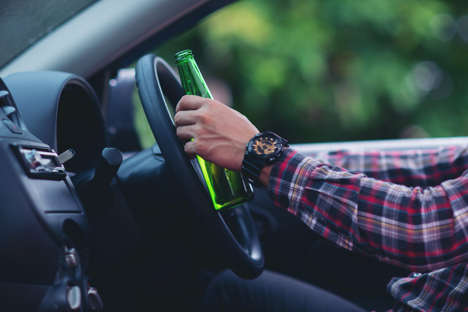 Asian Man Holds A Beer Bottle While Is Driving A Car
