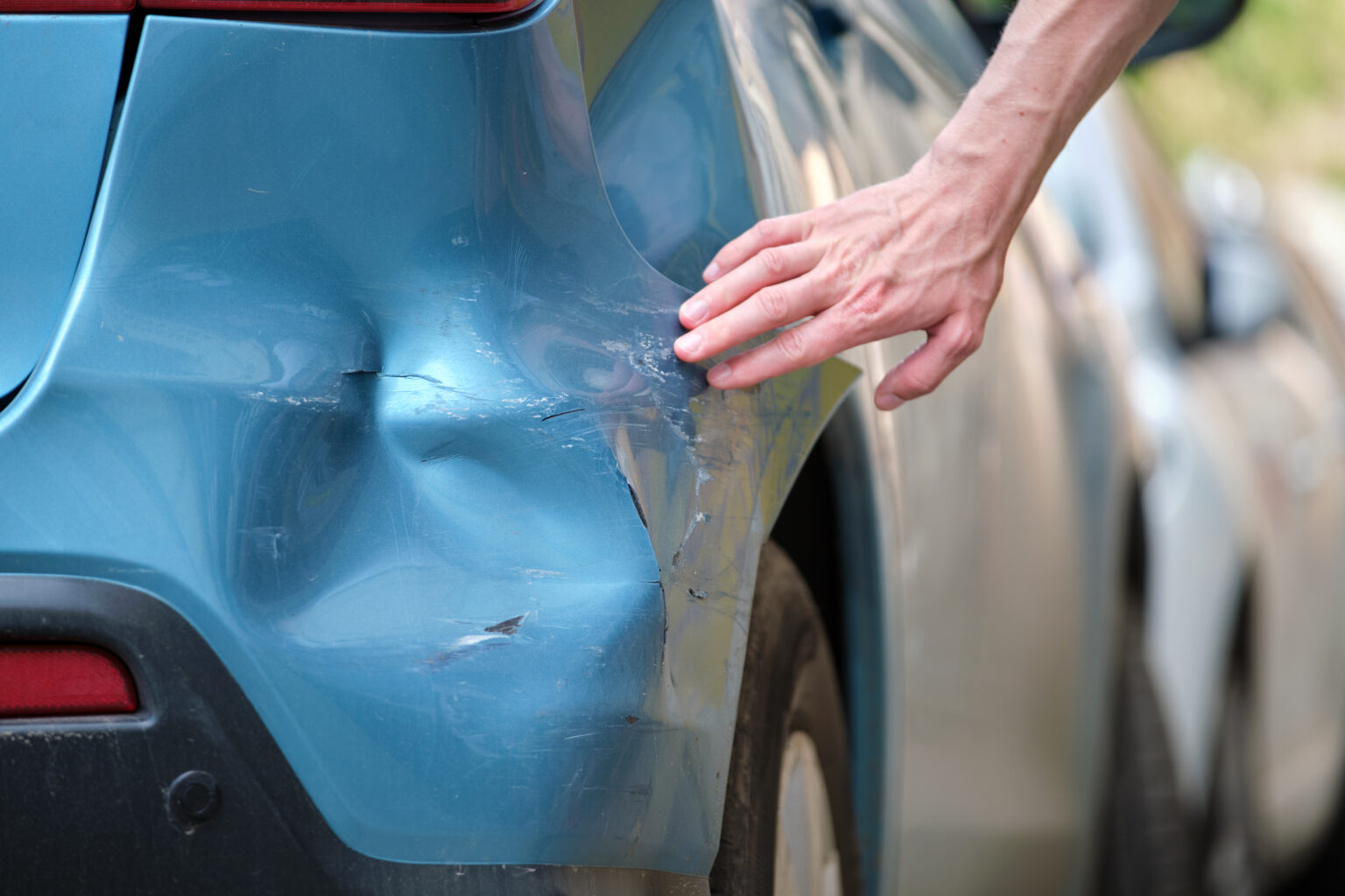 A Persons Hand Feeling The Dent On Their Blue Car