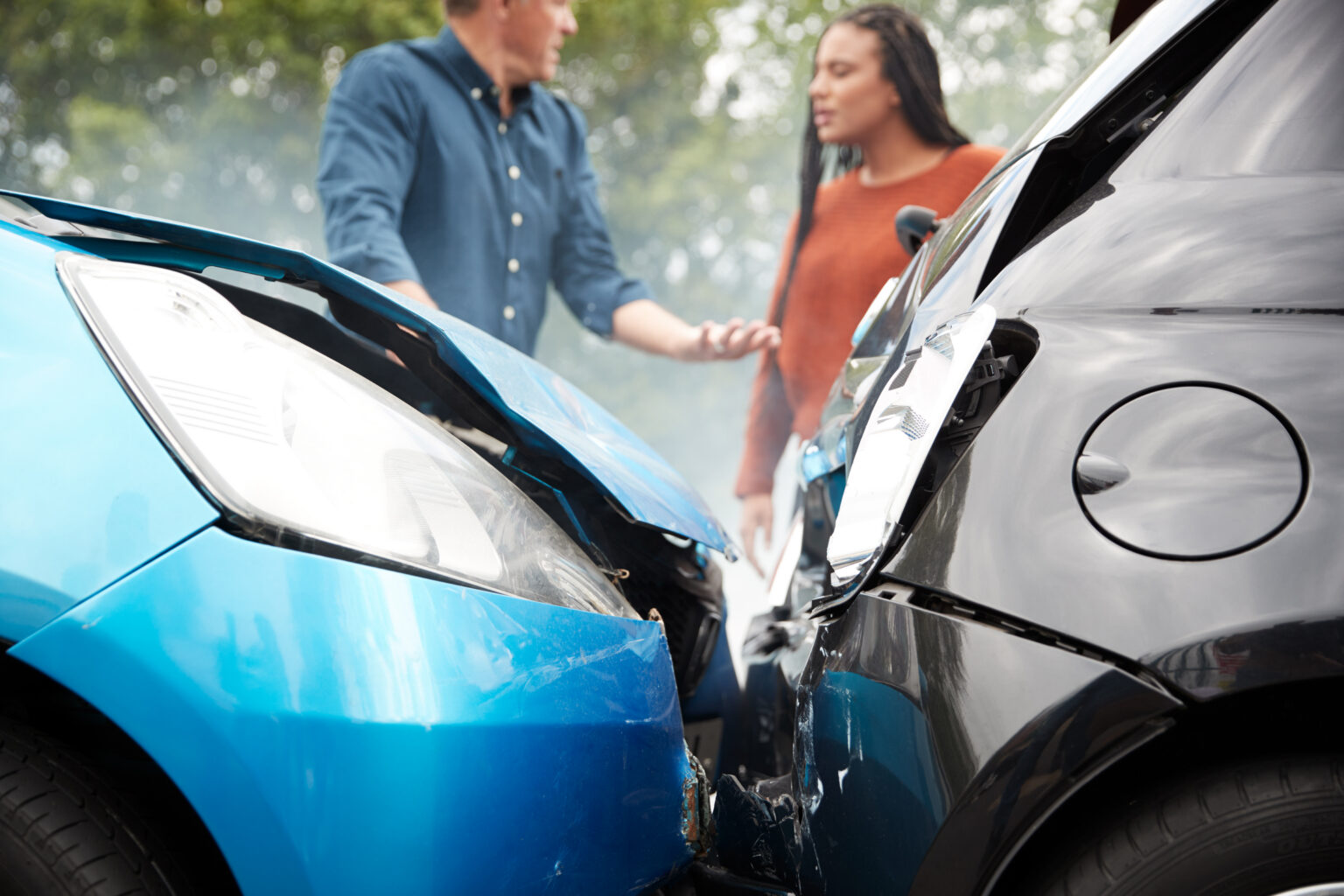 Close Up Of Two Cars Smashed Into Eachother With Two People Talking In The Background