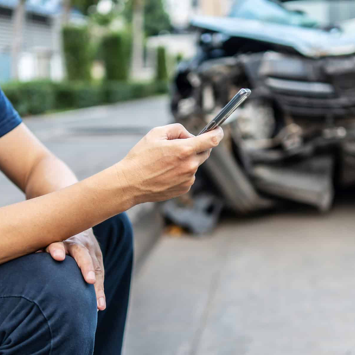 man calling with phone to his insurance agent after traffic accident with a background of the crashed car